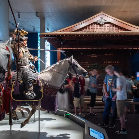 Ritterrüstungen auf Pferden in einem Museum, Besucher betrachten die Ausstellung.