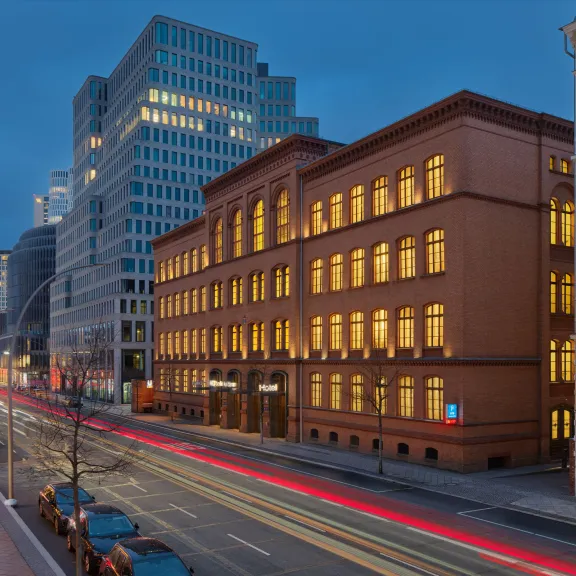 Abendliche Stadtstraße mit beleuchteten Bürogebäuden und Lichtstreifen vorbeifahrender Autos.