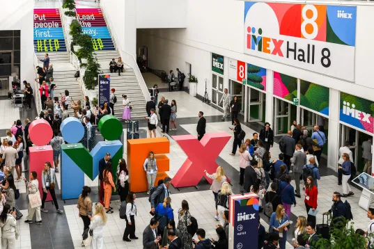 Viele Menschen auf einer Messe vor buntem IMEX-Logo und Eingang zur Halle 8.