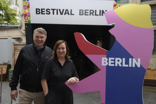 Zwei Personen stehen vor einem "Bestival Berlin" Schild und einer bunten Berliner Bär Figur.