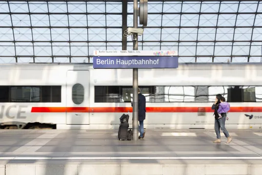 Zug am Bahnsteig im Berliner Hauptbahnhof, Menschen warten mit Gepäck.