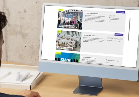 Mann sitzt am Schreibtisch und betrachtet Veranstaltungsliste auf Computerbildschirm.