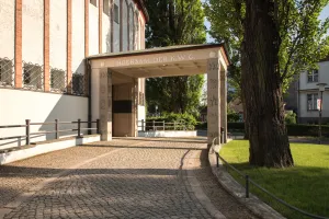 Eingang zu einem modernen Campusgebäude, umgeben von Bäumen und Grünflächen.