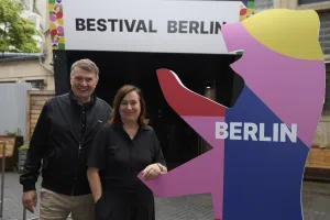 Zwei Personen stehen vor einem "Bestival Berlin" Schild und einer bunten Berliner Bär Figur.