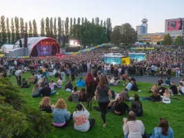 Menschenmenge bei Open-Air-Konzert auf einer Wiese vor einer großen Bühne im Park.