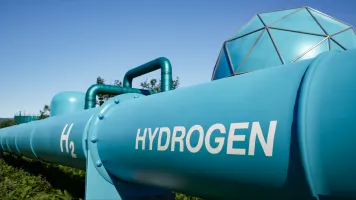 Große blaue Wasserstoffleitung mit der Aufschrift H₂ Hydrogen in einer Energieanlage bei blauem Himmel.