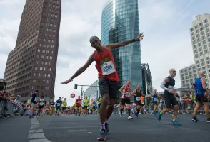 Läufer mit ausgebreiteten Armen beim Marathon in einer Stadt mit modernen Hochhäusern.