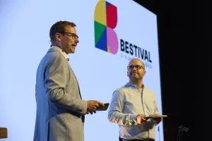 Zwei Männer stehen auf einer Bühne vor einer Leinwand mit dem Bestival-Logo.