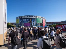 Menschenmenge vor Messegebäude bei sonnigem Wetter, bunte Werbebanner sichtbar