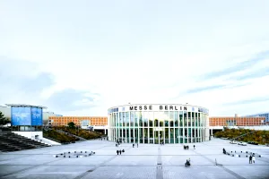 Glasfassade der Messe Berlin mit weitem Vorplatz und wenigen Besuchern.