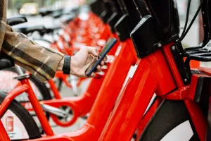 Person entsperrt mit dem Smartphone ein rotes Leihfahrrad an einer Fahrradstation.