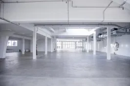 Leere, helle Lagerhalle mit weißen Wänden und Betonboden
