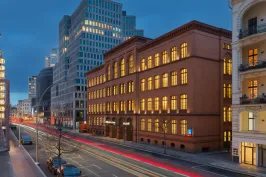 Abendliche Stadtstraße mit beleuchteten Bürogebäuden und Lichtstreifen vorbeifahrender Autos.