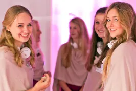  Zwei Hostessen in altrosa Kleidern lächeln in die Kamera, eleganter Promotion- und Empfangsservice vor rosa Kulisse bei Event und Markenpräsentation