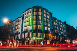 Beleuchtetes Hotelgebäude bei Nacht, vorbeifahrende Autos mit Lichtspuren.