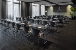 Moderner Konferenzraum mit Reihen aus schwarzen Tischen und Stühlen, Tageslicht durch Fenster.