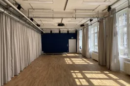 Heller Raum mit Holzfußboden, weißen Vorhängen und Sonnenlicht durch große Fenster.