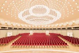Großer leerer Saal mit roten Stühlen und eindrucksvoller Deckenbeleuchtung.