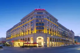 Großes, beleuchtetes Hotelgebäude an einer Straßenkreuzung bei Abenddämmerung.
