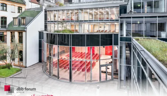 Moderne Glasfassade mit rundem Konferenzraum, innen rote Stühle, Außenansicht bei Tag.