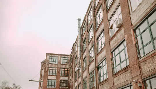 Backstein-Fabrikgebäude mit vielen Fenstern bei bewölktem Himmel
