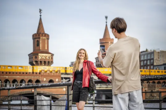 junges Paar macht Selfies auf der Oberbaumbrücke mit S-Bahn im Hintergrund