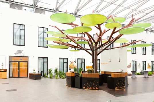 Großer künstlicher Baum mit grünen Blättern in modernem, hellem Innenhof