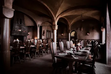 Großer, dämmrig beleuchteter Speisesaal mit langen Holztischen und Gewölbedecke.