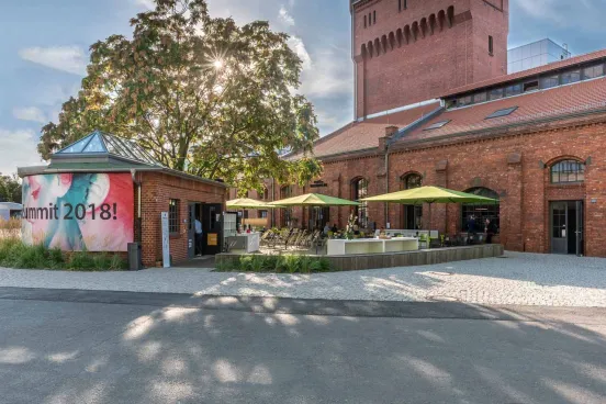 Backsteinbau mit Terrasse, Sonnenschirmen und Bäumen im Sonnenschein
