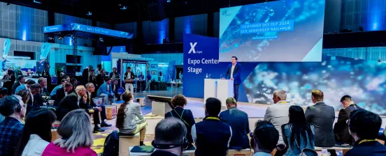 Ein Sprecher auf der Bühne der X Expo, vor ihm sitzt ein interessiertes Publikum.