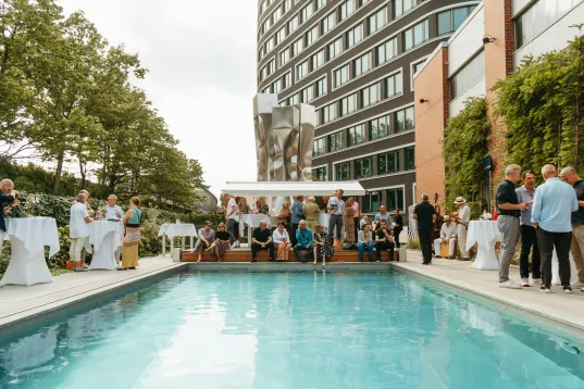 Menschen feiern entspannt an einem Pool neben einem modernen Gebäude.