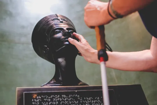 Während der Ausstellung „Im Licht von Amarna“, eine Frau tastet eine Figure mit den Händen ab