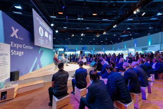 Teilnehmende sitzen vor einer kleinen Bühne, die als Expo Stage gekennzeichnet ist
