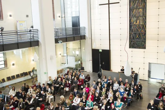 Große Gruppe von Menschen sitzt in einer modernen, hellen Kirche mit hohen Decken.