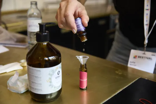 Person tropft Flüssigkeit aus einer kleinen Flasche durch einen Trichter in ein braunes Glasfläschchen.