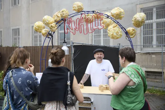 Ein Popcornstand an dem drei Personen stehen und dem Standbetreiber zuhören
