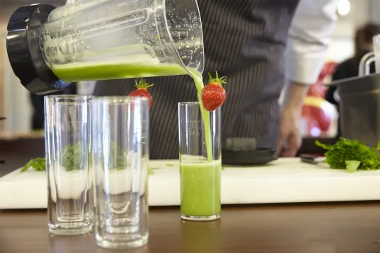 Auf dem Bild ist ein grüner Saft von einem Mixer in das Glas geschüttet