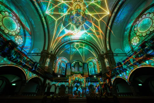 Bunte Lichtprojektionen an Decke und Wänden einer großen Kirche mit Rundfenstern